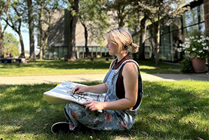 Woman sitting on grass with canvas on lap